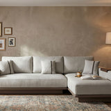 Japandi-inspired L-shaped sofa with built-in side shelf armrest in walnut wood, upholstered in light grey fabric with plush back cushions